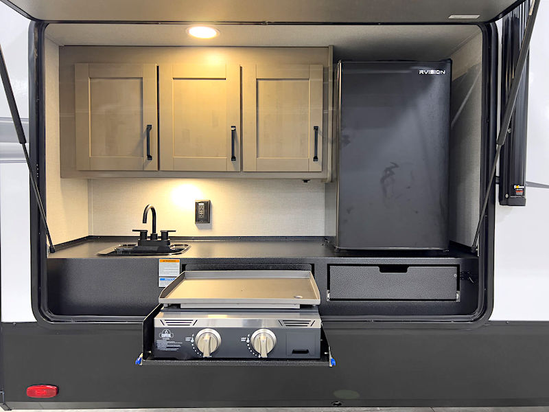 outside kitchen on a camper trailer with a fridge, griddle, sink, cabinetry and lighting