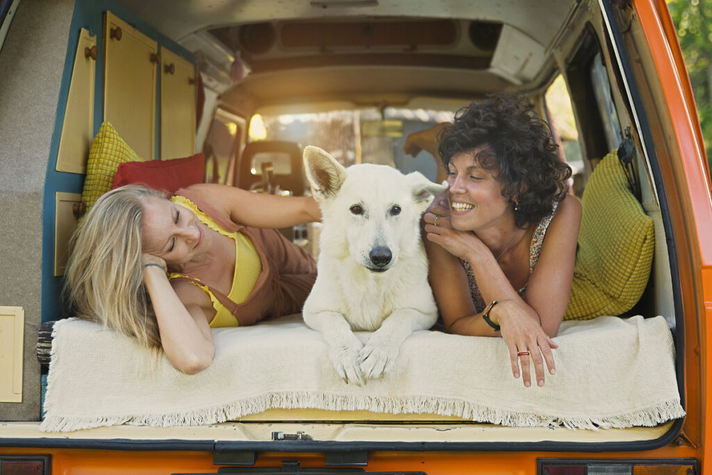 Two woman and a white dog laying in the back of a van