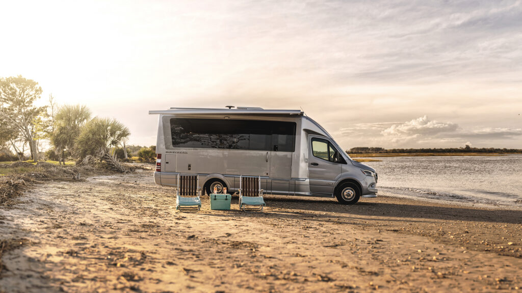 The 2022 Airstream Atlas Class B RV parked on a beach with 2 lounge chairs in the foreground. How much does a campervan cost?