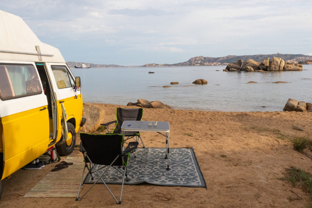 Yellow campervan parked next to the ocean with a camp set up