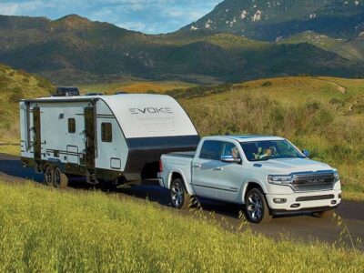 White truck towing a travel trailer in grass covered hills