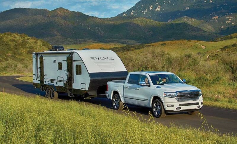 White truck towing a travel trailer in grass covered hills