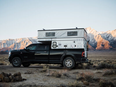 Crew cab truck with a pop-up truck camper parked near the mountains