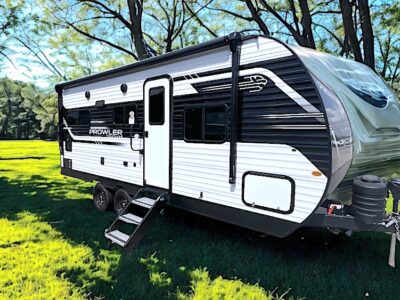 Heartland Prowler 2103MKS in a green field with some trees around and a blue sky